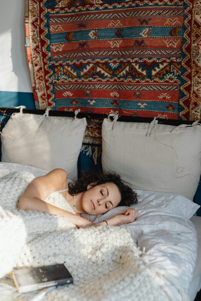 Woman sleeping peacefully in a cozy bedroom with decorative tapestry on wall.